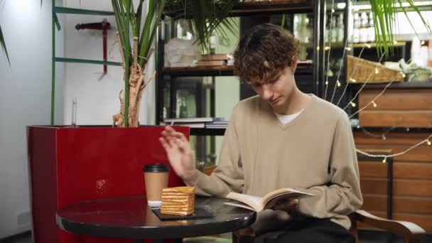 Close-up de um cara sentado em um café, tomando café e lendo um livro. Trabalho fora de casa — Vídeo de Stock