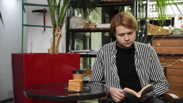 Close-up de um cara sentado em um café, tomando café e lendo um livro. Trabalho fora de casa — Vídeo de Stock