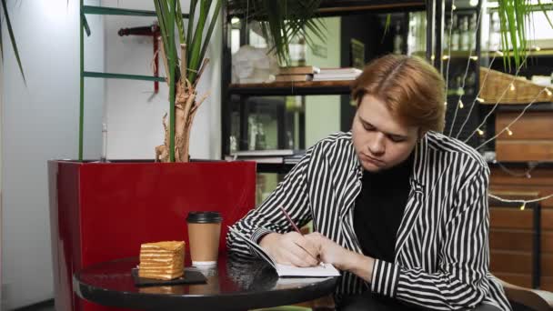Κοντινό πλάνο ενός τύπου που κάθεται σε ένα καφέ και γράφει σε ένα σημειωματάριο. Καφέ — Αρχείο Βίντεο