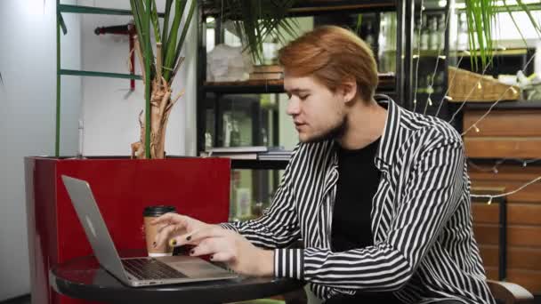 Close-up van een man die in een café zit met een laptop aan een tafel, koffie drinkt en via een videolink praat. Buiten het huis werken — Stockvideo