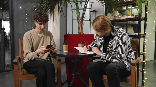 Two gay guys on a date are sitting in a coffee shop. The guy draws in his partner s notebook. LGBT — Stock Photo, Image