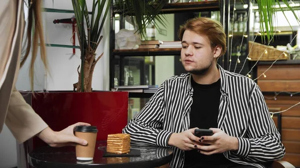 Close-up de um cara sentado em um café e digitando uma mensagem em seu telefone. A garçonete traz café ao cara. Cafeteira — Fotografia de Stock