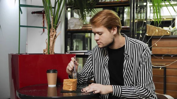 Close-up de um tipo sentado num café. O tipo come bolo de mel e bebe café num aconchegante café. Cafeteira — Fotografia de Stock