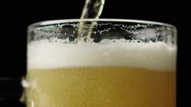 Siyah bir arka planda cam bir fincanın içine bira dökme ve köpürme yakın plan
