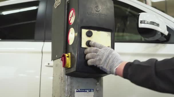 De automonteur drukt op een knop op het hef- en transportmechanisme van de krik om de auto te laten zakken. Auto reparatie, reparatie, onderhoud — Stockvideo