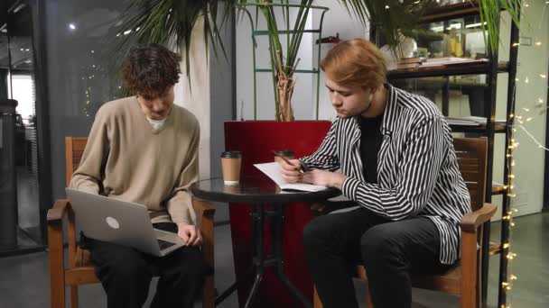 Två bögar på en dejt sitter på ett kafé, dricker kaffe och tittar på något på en bärbar dator. HBTQ — Stockvideo