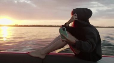 Bir kadın gün batımında motorlu bir teknede kendi fotoğrafını çekiyor.