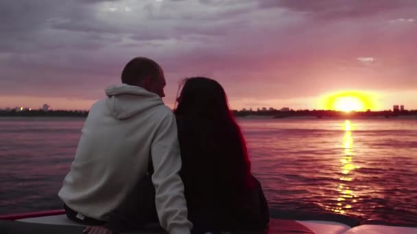A guy and a girl are sitting in a motor boat and watching the sunset. Romantic atmosphere. — Stock Video