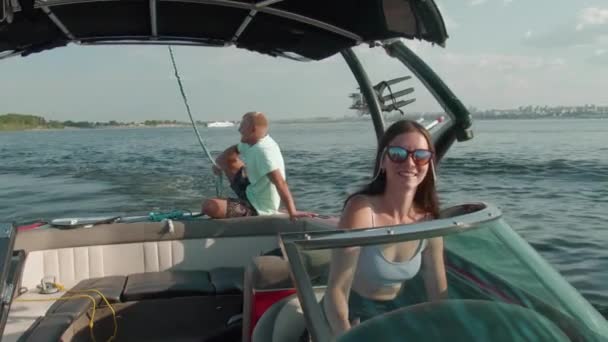 Una mujer está conduciendo un barco a motor, y un hombre está sentado en el fondo y disfrutando del agradable aire fresco — Vídeos de Stock