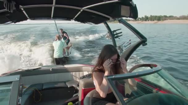 Une femme conduit un bateau à moteur, et en arrière-plan un gars monte un wakeboard, et l'homme l'aide — Video