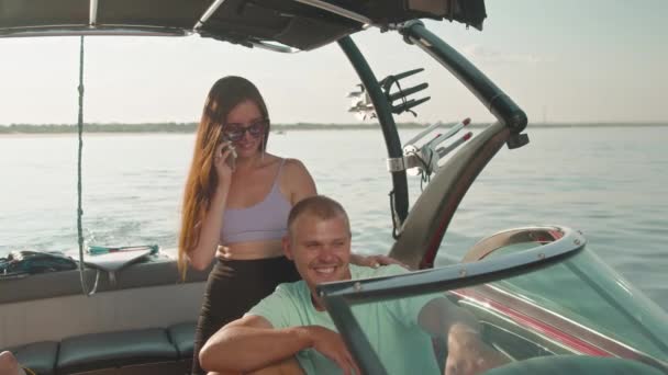男がモーターボートに座っていて、隣に女性が立って電話で話している。 — ストック動画