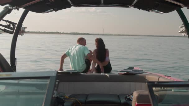 Um cara e uma menina estão sentados em um barco a motor, beijando e olhando para a distância. Ambiente romântico. — Vídeo de Stock