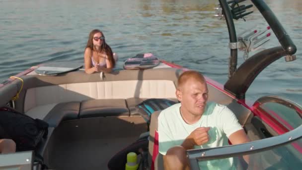 Bir adam motorlu tekne kullanıyor ve arka planda bir kadın yüzüstü uzanıyor ve güzel havanın tadını çıkarıyor. — Stok video
