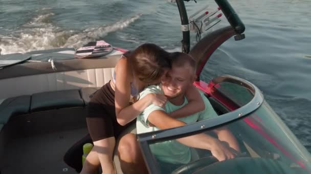 Muž řídí motorový člun a žena k němu přistoupí a zezadu ho obejme. — Stock video
