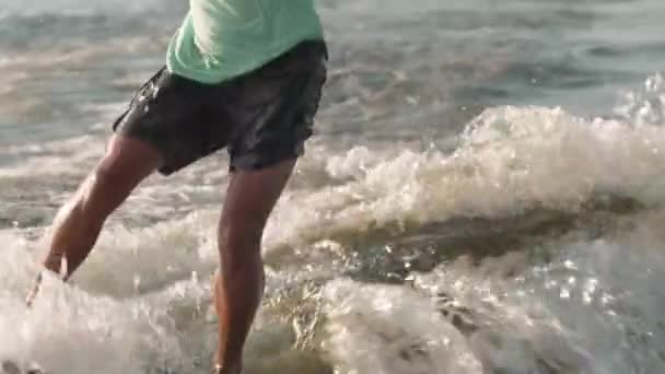 Een surfer die op een wakeboard springt drinkt uit een beker. Een ervaren wakeboarder spat water in de camera. — Stockvideo