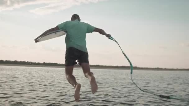 Muž s wakeboardem skočí do vody — Stock video