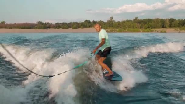 Een surfer springt op een wakeboard. Een ervaren wakeboarder spuit waterdruppels in de camera. — Stockvideo