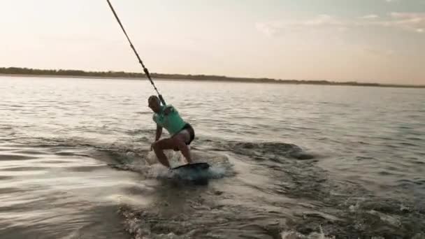 Ένας σέρφερ που πηδάει σε μια σανίδα. Ένας έμπειρος wakeboarder ψεκάζει νερό σταγόνες στην κάμερα. — Αρχείο Βίντεο