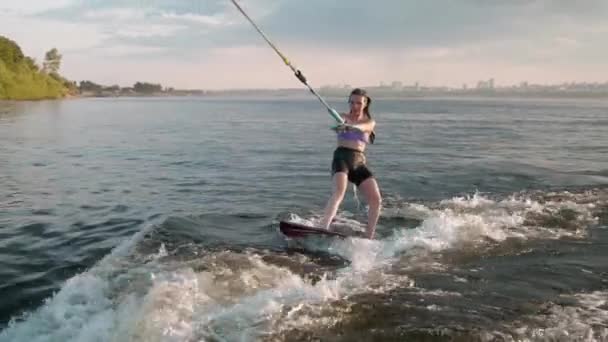 Samica surfera skacząca na desce. Doświadczony wakeboarder chlapie krople wody do kamery. — Wideo stockowe