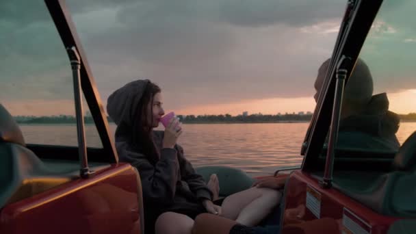 Um tipo e uma rapariga sentados num barco a motor a falar e a ver o pôr-do-sol. Ambiente romântico. — Vídeo de Stock