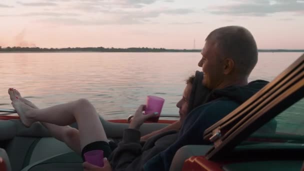 Egy fiú és egy lány ölelkeznek napnyugtakor egy csónakban ülve. — Stock videók