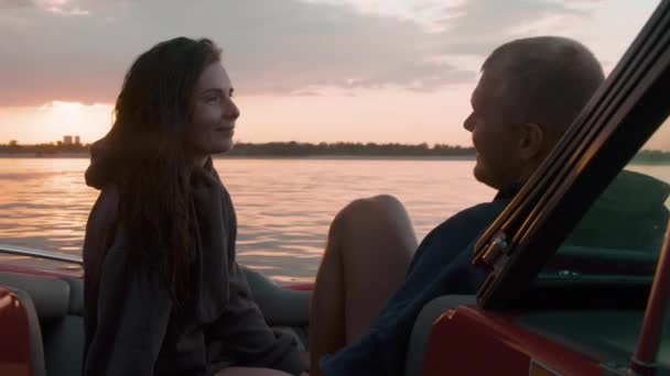 Um cara e uma menina abraçar bonito ao pôr do sol sentado em um barco — Vídeo de Stock