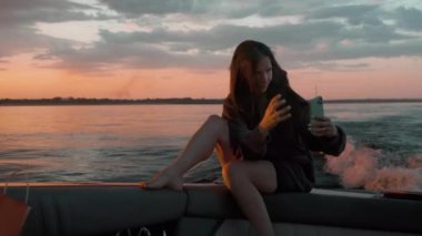 Bir kadın gün batımında motorlu bir teknede kendi fotoğrafını çekiyor.