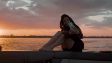 Bir kadın gün batımında motorlu bir teknede kendi fotoğrafını çekiyor.