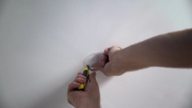 Tanımlanamayan bir erkek elektrikçinin yakın plan fotoğrafı. Geleceğin lambası için delik açıyor. Aydınlatma armatürlerinin kurulumu, tavanın altındaki kablolar.