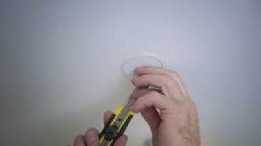 Tanımlanamayan bir erkek elektrikçinin yakın plan fotoğrafı. Geleceğin lambası için delik açıyor. Aydınlatma armatürlerinin kurulumu, tavanın altındaki kablolar.