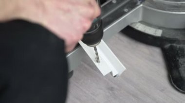 Erkek ellerine yakın çekim. Bir işçi, beyaz plastik bir çubukta delik açmak için kablosuz matkap kullanır. İşçi kazı yapıyor..