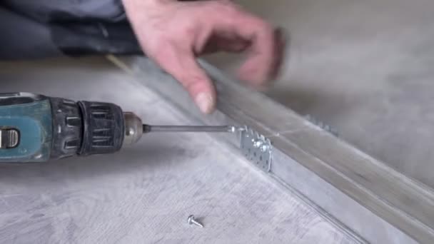 Närbild av manliga händer. En arbetare använder en sladdlös borr för att borra ett hål i en mörkgrå metallpinne. Handyman borrar installation. — Stockvideo