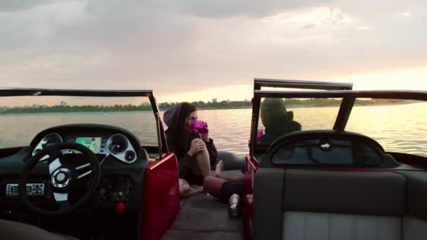 Facet i dziewczyna siedzą na motorówce, rozmawiają i oglądają zachód słońca. Romantyczna atmosfera. — Wideo stockowe