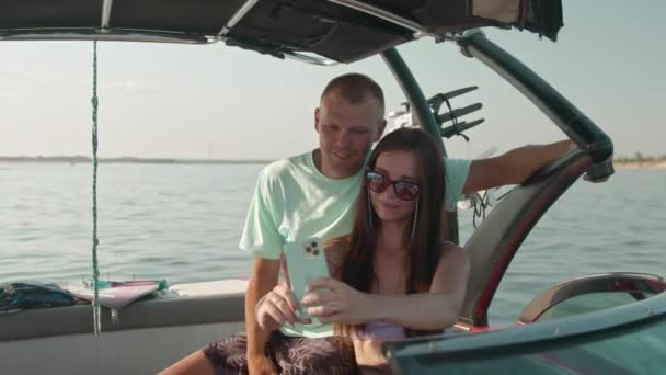 Um homem e uma mulher estão sentados em um barco a motor e tirando fotos — Vídeo de Stock