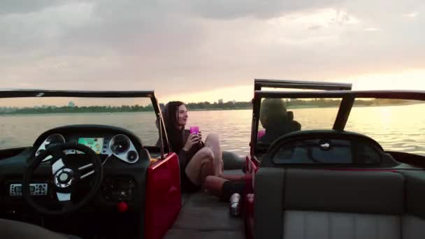 A guy and a girl are sitting in a motor boat kissing and watching the sunset. Romantic atmosphere. — Stock Video