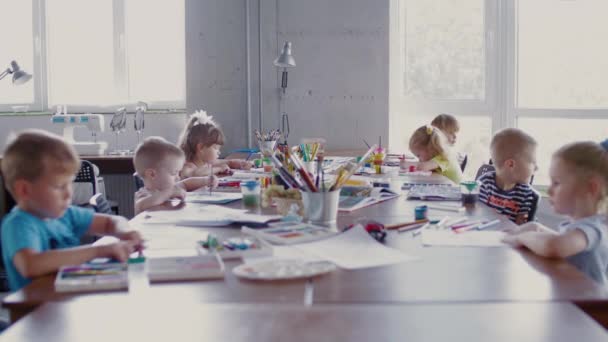 I bambini si siedono a tavola e disegnano su carta con colori e pennelli diversi — Video Stock