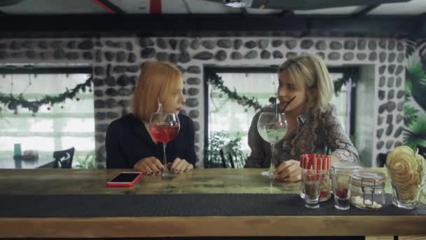 Dos chicas están sentadas en un bar charlando y recibiendo sus cócteles del camarero — Vídeo de stock