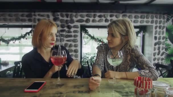 Twee meisjes zitten in een bar te kletsen en krijgen hun cocktails van de barman. — Stockvideo