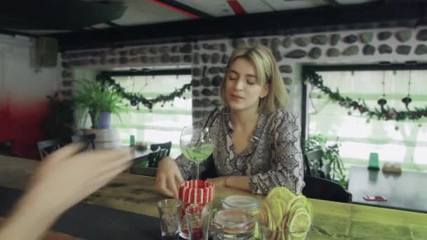Una chica está sentada en un bar con una copa de vino en las manos y se comunica con el camarero. — Vídeos de Stock