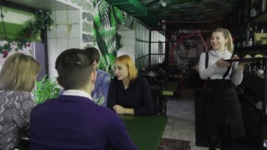 Bir grup arkadaş bir barda bir masada oturuyor. Garson kız siparişleri getiriyor..