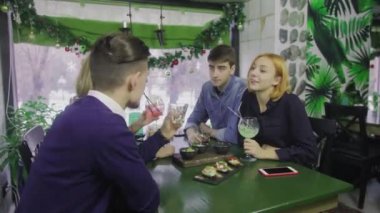 Bir grup arkadaş bir barda bir masada oturuyor. Genç bir adam kadeh kaldırır, herkes bardaklarını tokuşturur ve alkollü kokteyllerini içer..