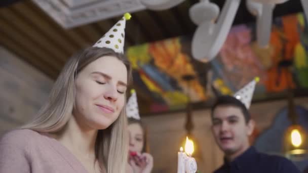 Zbliżenie dziewczyny zdmuchującej świeczki na torcie. solenizantka zachwycona urodzinami z najlepszymi przyjaciółmi — Wideo stockowe