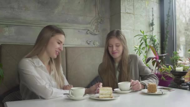 Twee vriendinnen drinken koffie, praten en lachen terwijl ze aan een tafel zitten in een café. — Stockvideo