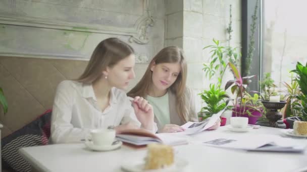 Twee meisjes zitten aan een tafel in een café en lossen zakelijke problemen op. Werken buiten het huis — Stockvideo