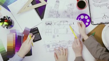 İki kadın tasarımcı bir masada araba çizimlerini tartışıyor ve hesap makinesine güveniyor.