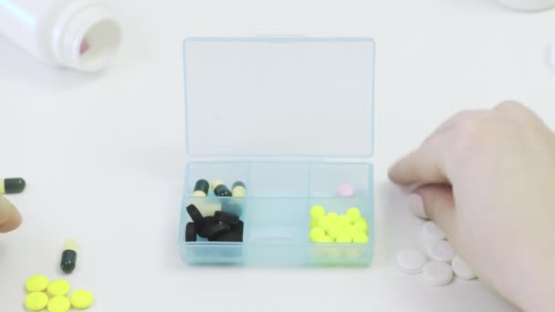 Close-up de um pillbox com comprimidos diferentes. As mãos de uma pessoa põem pílulas em um pillbox — Vídeo de Stock