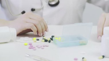 Farklı tabletlerle bir ilaç kutusuna yakın çekim. Bir insan eli ilaç kutusuna koyar.