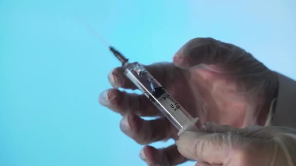 Close-up de uma agulha de uma seringa descartável. Uma seringa pequena empurra o líquido para fora do buraco sobre um fundo azul — Vídeo de Stock