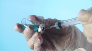 Doktorun elleri mavi arka planda aşı için aşı hazırlıyor.