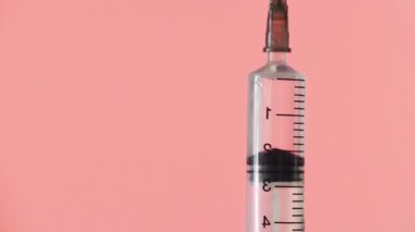 Tek kullanımlık şırınganın iğnesinin yakın çekimi. Bir insan eli kırmızı arka plandaki şırınganın kapağını açar.